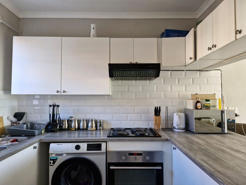 A functional kitchen featuring white cabinetry, a subway tile backsplash, wood-look laminate countertops, and integrated appliances including an oven and hob.