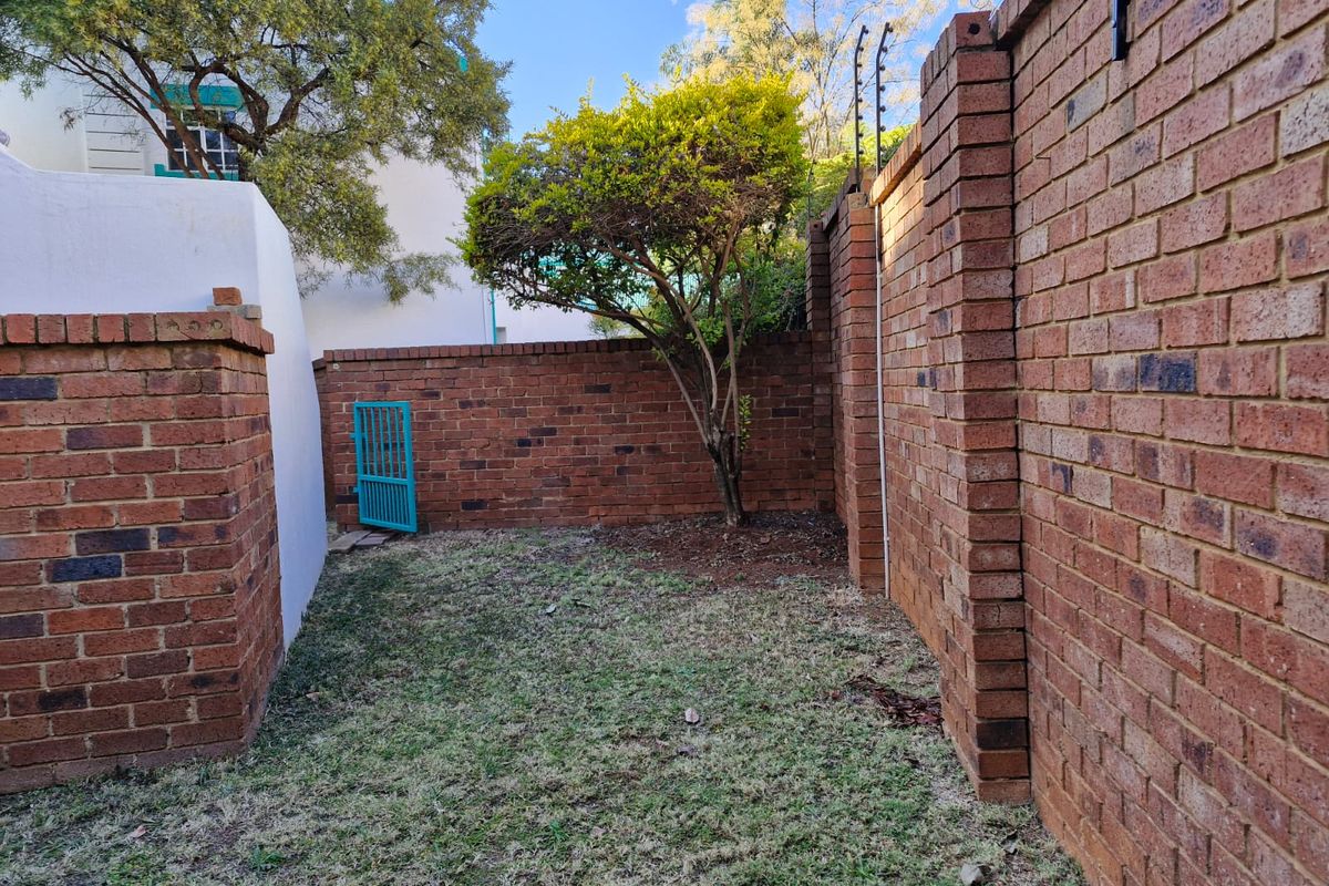 A private rear garden area enclosed by high brick boundary walls featuring integrated electric fencing and a small metal pedestrian access gate.
