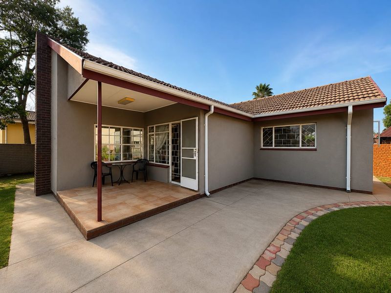Rear view of the property featuring a covered tiled patio, concrete paving, and well-maintained exterior walls with security bars on windows.