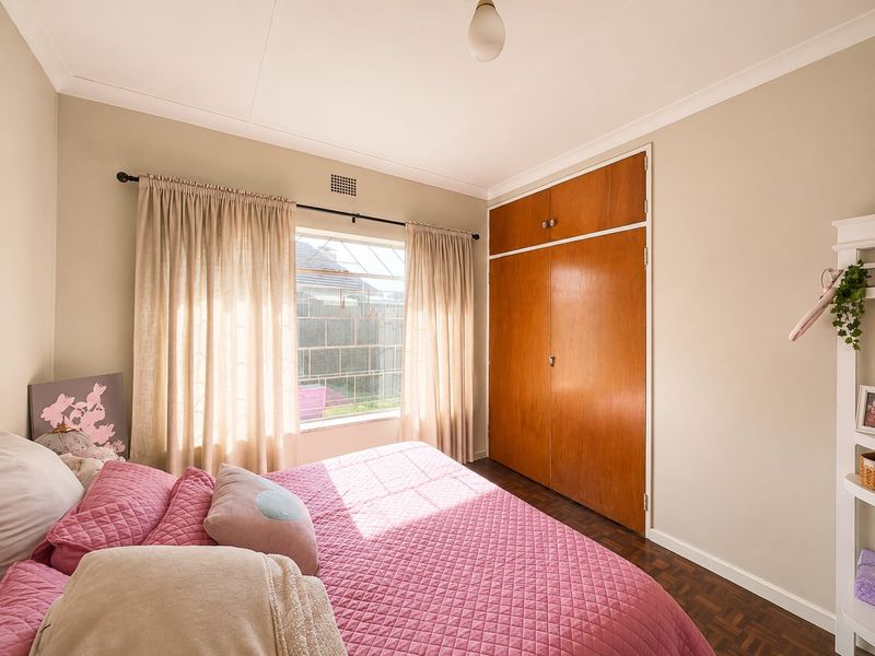 A bedroom featuring parquet flooring, a built-in wooden wardrobe, and a window with security bars, offering a functional and well-lit living space.