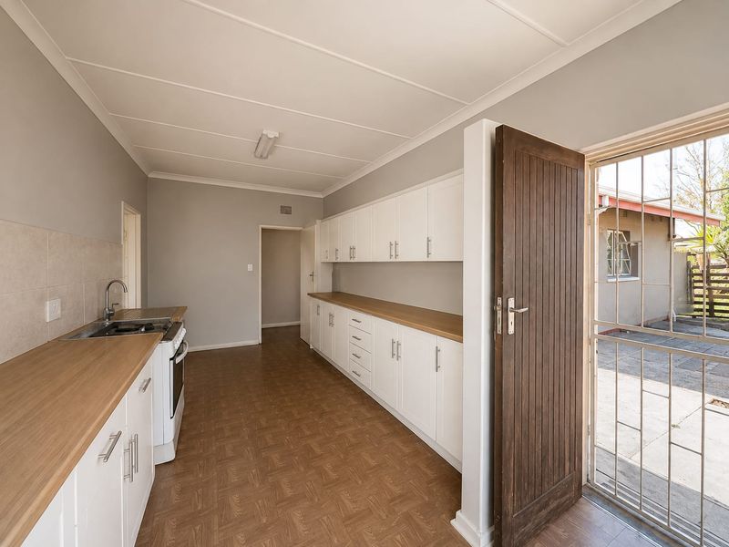 A clean, functional kitchen featuring white cabinetry, wood-look laminate countertops, and direct access to the exterior via a secure timber door.