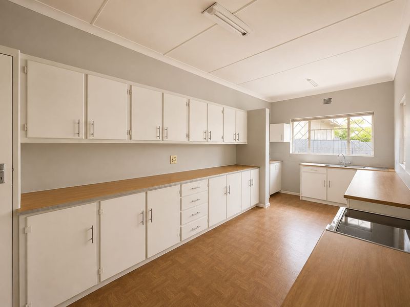 A functional, empty kitchen featuring extensive white cabinetry, laminate countertops, a built-in hob, and a stainless steel sink with a window view.