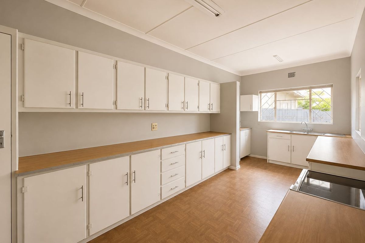 A functional, empty kitchen featuring extensive white cabinetry, laminate countertops, a built-in hob, and a stainless steel sink with a window view.