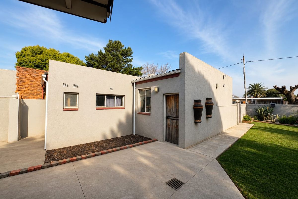 A well-maintained rear exterior view featuring a concrete patio, manicured lawn, and a stucco-finished building facade with timber door and casement windows.