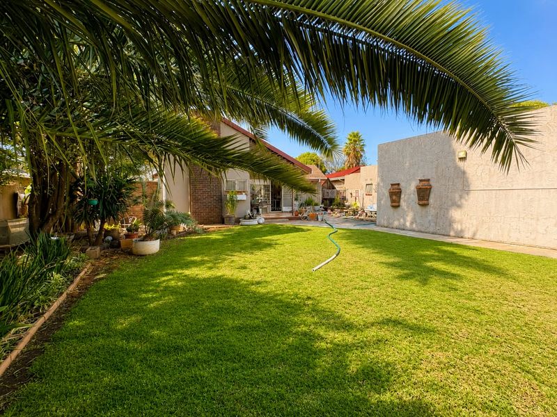 A spacious rear garden featuring a well-maintained lawn, mature palm tree, and a private courtyard area with brick and stucco wall finishes.