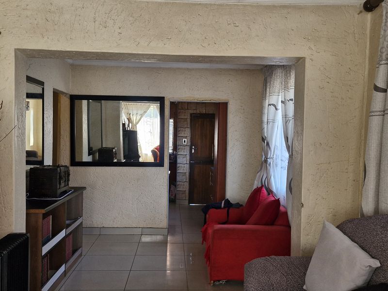 A living room area featuring tiled flooring and textured walls, providing a functional space with direct access to adjacent rooms.