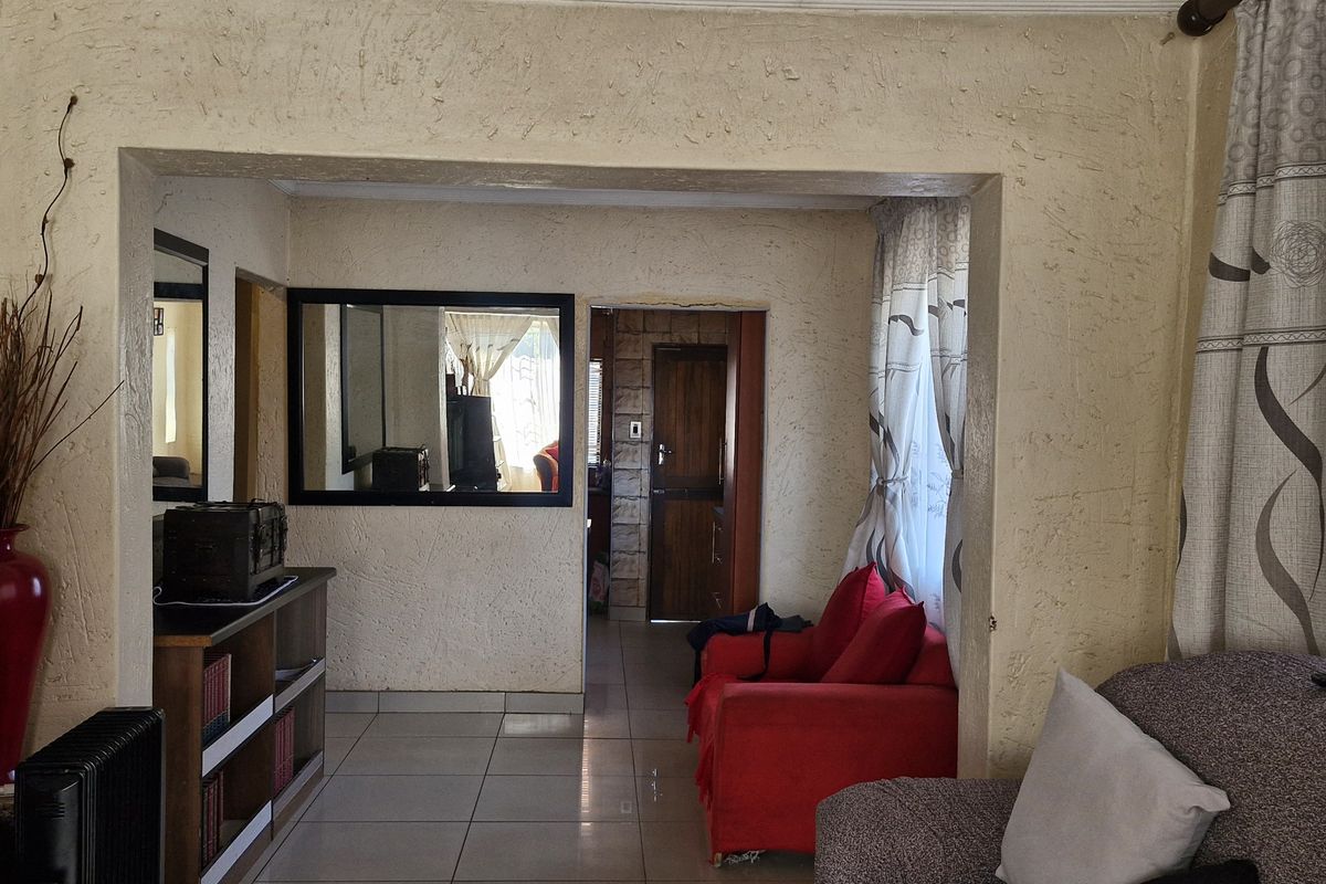 A living room area featuring tiled flooring and textured walls, providing a functional space with direct access to adjacent rooms.