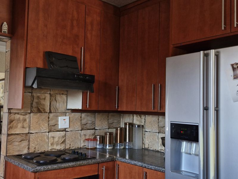 A functional kitchen featuring wood-finish cabinetry, a stone-look tile backsplash, and integrated cooking appliances, with an open-plan flow into the adjacent living area.