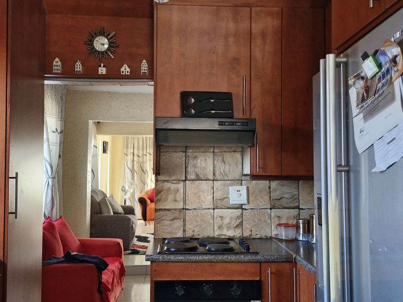 A functional kitchen featuring wood-finish cabinetry, a tiled backsplash, and integrated cooking appliances, with a view through to the adjacent living area.