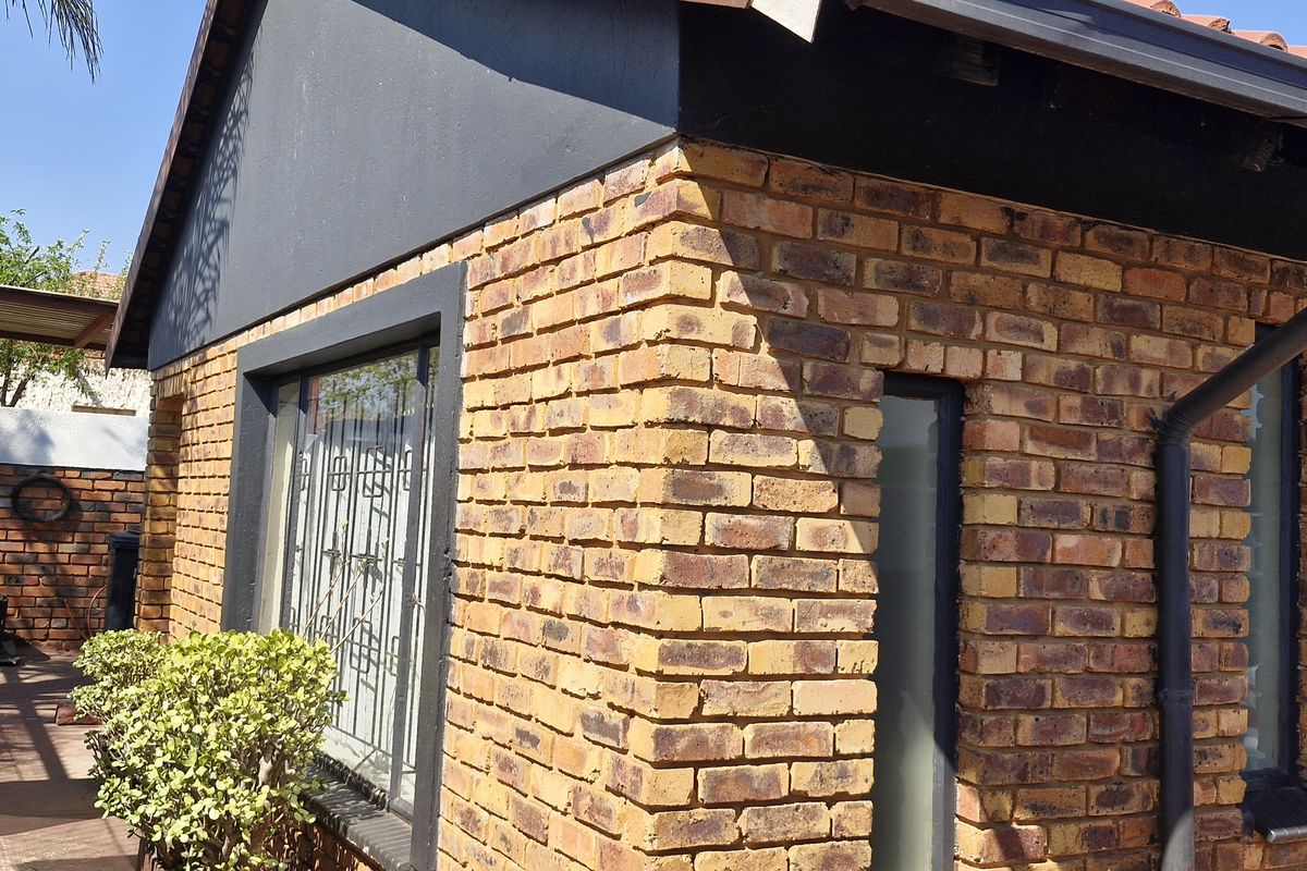 A view of the rear exterior featuring face brick walls, a tiled roof, and a paved side walkway with security bars on the windows.