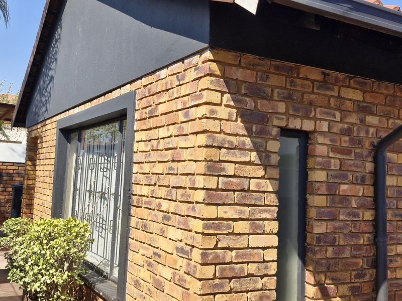 A view of the rear exterior featuring face brick walls, a tiled roof, and a paved side walkway with security bars on the windows.