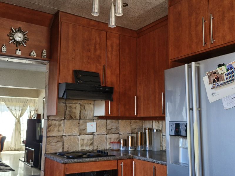 A functional kitchen featuring warm-toned wooden cabinetry, a tiled backsplash, and built-in cooking appliances, with an open flow into the adjacent living area.