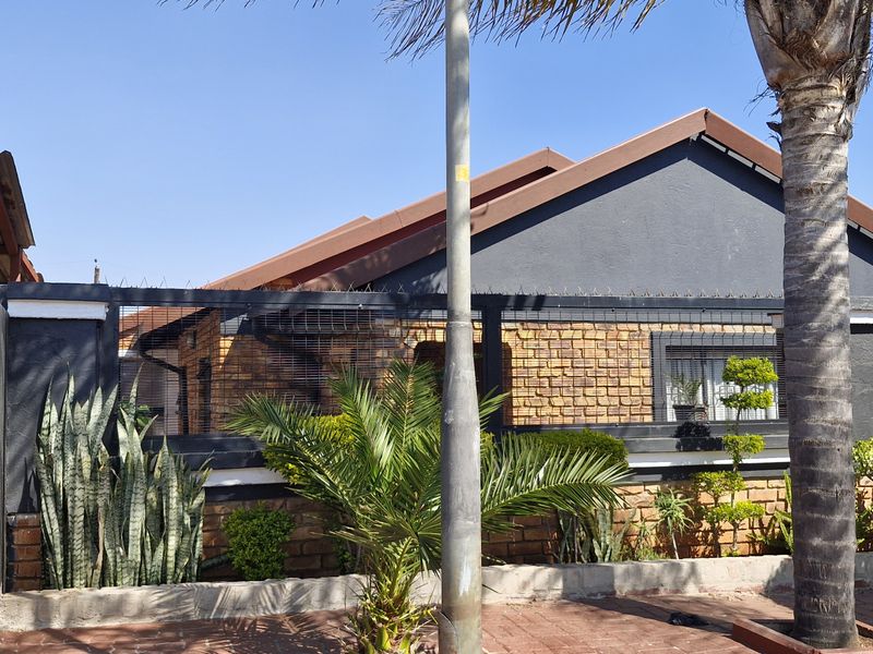 Front elevation of a face brick house featuring a tiled roof, secure perimeter fencing with razor wire, and an adjacent carport structure.