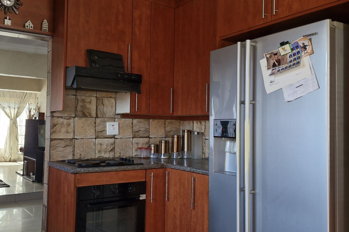 A functional kitchen featuring wood-finish cabinetry, tiled backsplash, and built-in cooking appliances, with an open-plan flow into the adjacent living area.