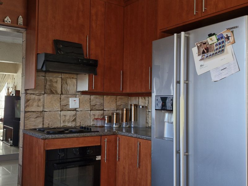 A functional kitchen featuring wood-finish cabinetry, tiled backsplash, and built-in cooking appliances, with an open-plan flow into the adjacent living area.
