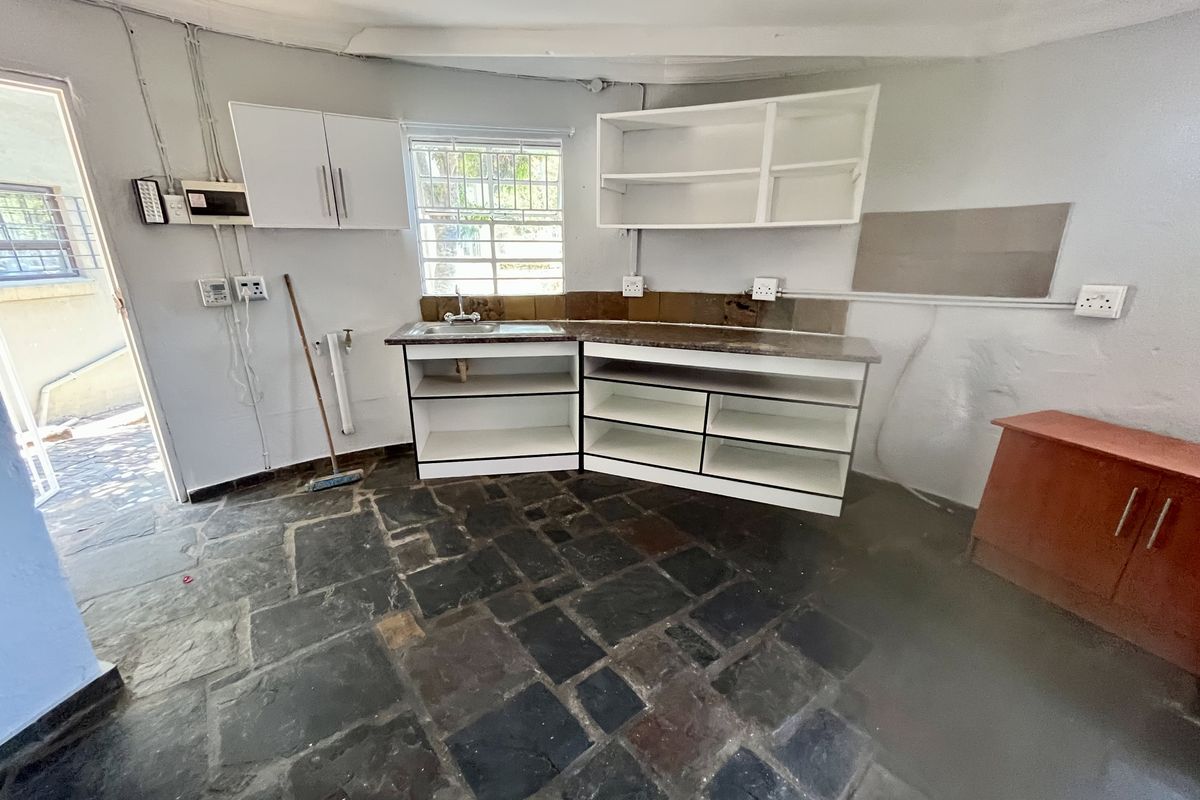 A functional kitchen space featuring stone flooring, built-in cabinetry, and a stainless steel sink, offering potential for modernization and renovation.
