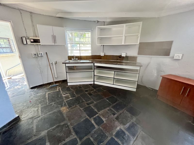A functional kitchen space featuring stone flooring, built-in cabinetry, and a stainless steel sink, offering potential for modernization and renovation.