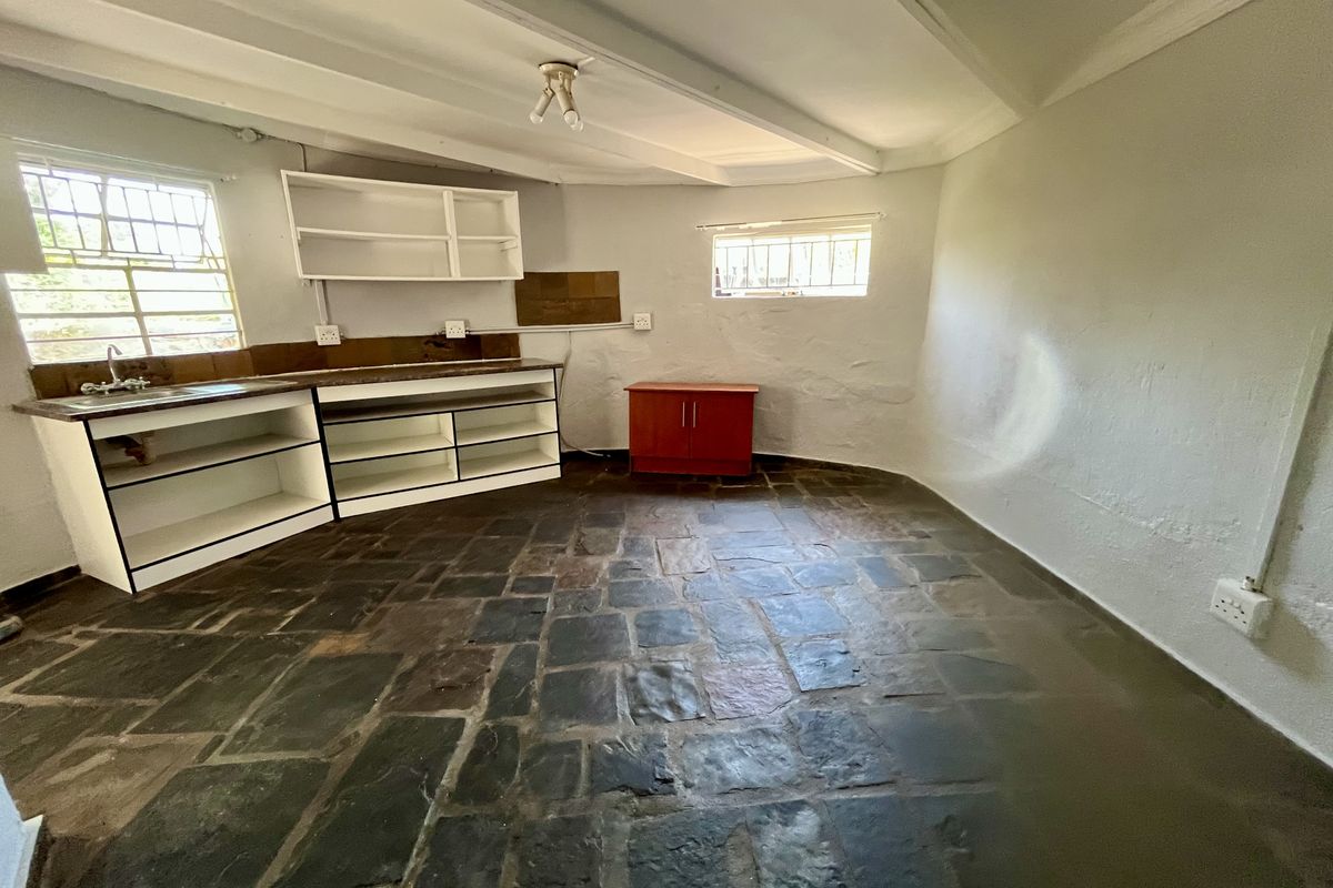 A rustic kitchen area featuring stone flooring, built-in cabinetry, and exposed ceiling beams, offering a blank canvas for renovation and modernization.