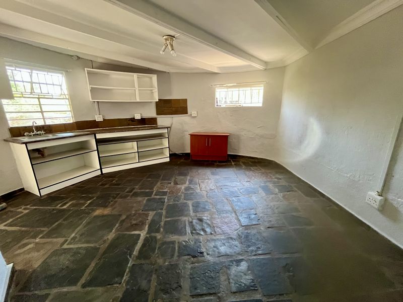 A rustic kitchen area featuring stone flooring, built-in cabinetry, and exposed ceiling beams, offering a blank canvas for renovation and modernization.