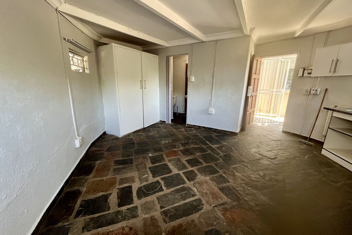 Open plan living area featuring rustic stone flooring, exposed ceiling beams, built-in storage, and direct access to an exterior security gate.