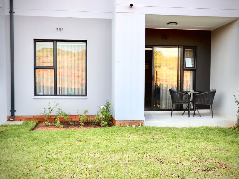 A well-maintained rear exterior view of the apartment featuring a covered patio, sliding glass doors, and a private garden area.