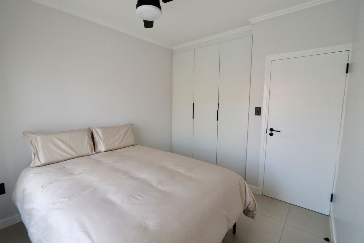 A clean and well-maintained bedroom featuring neutral tiled flooring, built-in cupboards, and a ceiling fan.