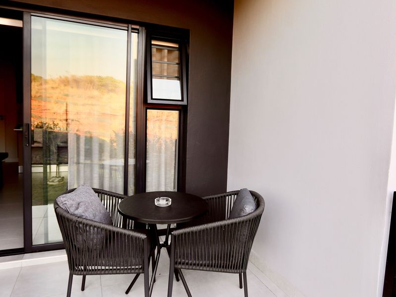 A modern, covered balcony featuring tiled flooring, a sliding glass door, and a sleek, dark-toned accent wall.