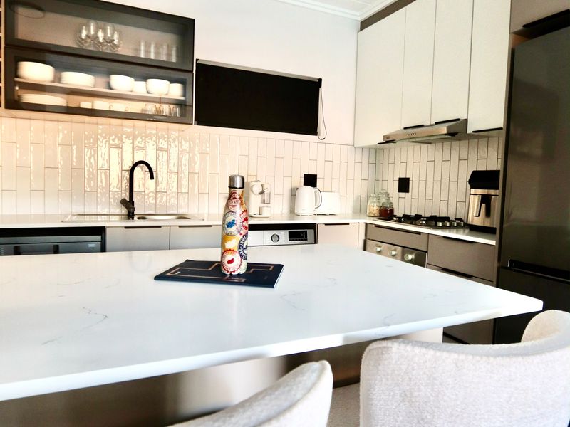 Modern kitchen featuring white quartz countertops, subway tile backsplash, sleek cabinetry, and integrated appliances with a central island breakfast bar.