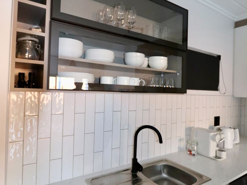 Modern kitchen area featuring a clean white subway tile backsplash, quartz countertops, a sleek black faucet, and contemporary glass-front cabinetry.