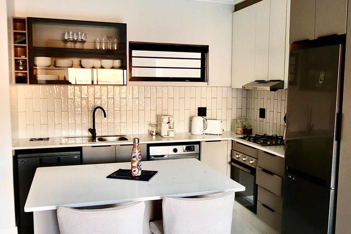 Modern kitchen featuring sleek cabinetry, stone countertops, subway tile backsplash, a central island, and integrated appliances including a gas hob and oven.