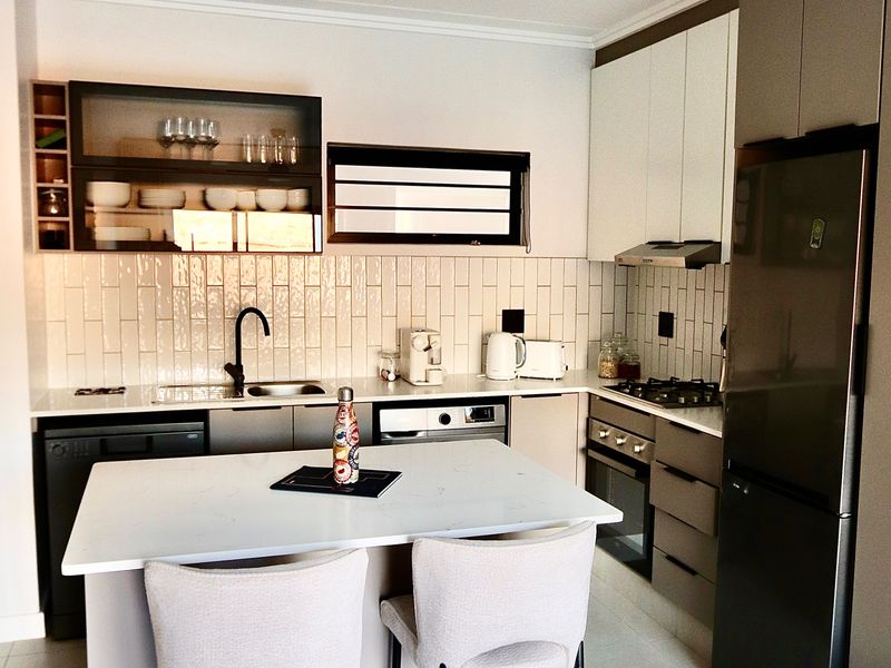 Modern kitchen featuring sleek cabinetry, stone countertops, subway tile backsplash, a central island, and integrated appliances including a gas hob and oven.