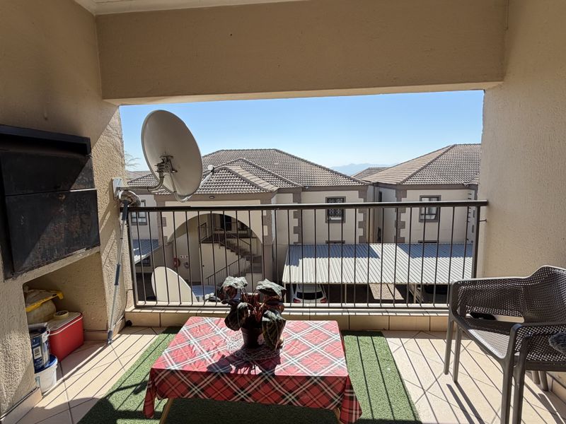 Covered balcony featuring a built-in braai, tiled flooring, and a metal balustrade overlooking the complex grounds.
