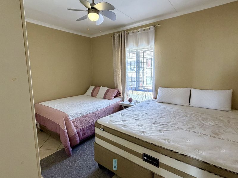 A functional bedroom featuring tiled flooring, a ceiling fan, and security bars on the window, providing a practical space for rest.