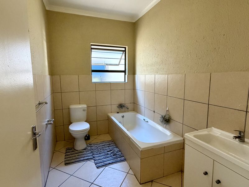 A functional bathroom featuring a built-in bathtub, toilet, and vanity cabinet with neutral ceramic tiling throughout.