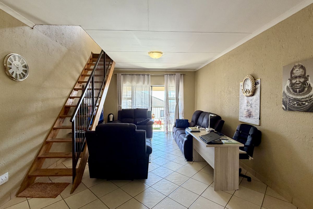 Open-plan living area featuring ceramic floor tiles, a wooden staircase with metal railing, and access to an outdoor balcony through sliding glass doors.