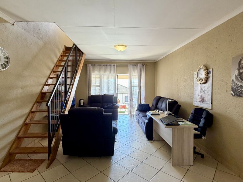 Open-plan living area featuring ceramic floor tiles, a wooden staircase with metal railing, and access to an outdoor balcony through sliding glass doors.