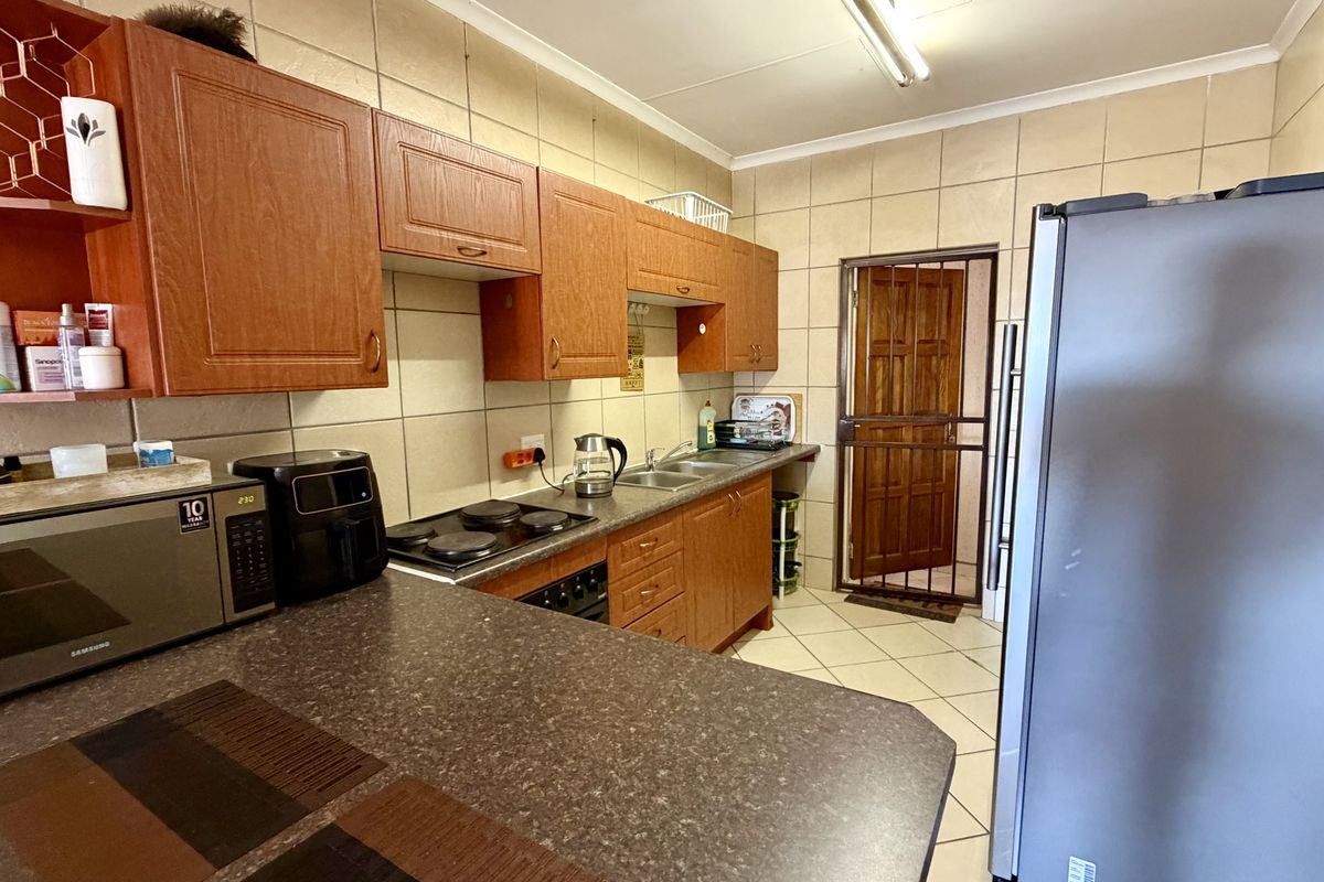 A functional kitchen featuring wood-finish cabinetry, laminate countertops, an electric hob, and tiled surfaces, providing a practical layout for daily meal preparation.