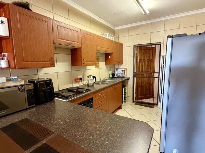 A functional kitchen featuring wood-finish cabinetry, laminate countertops, an electric hob, and tiled surfaces, providing a practical layout for daily meal preparation.