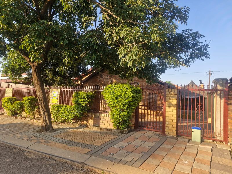 Front view of the property featuring a brick boundary wall, metal security fencing, and a paved driveway entrance.