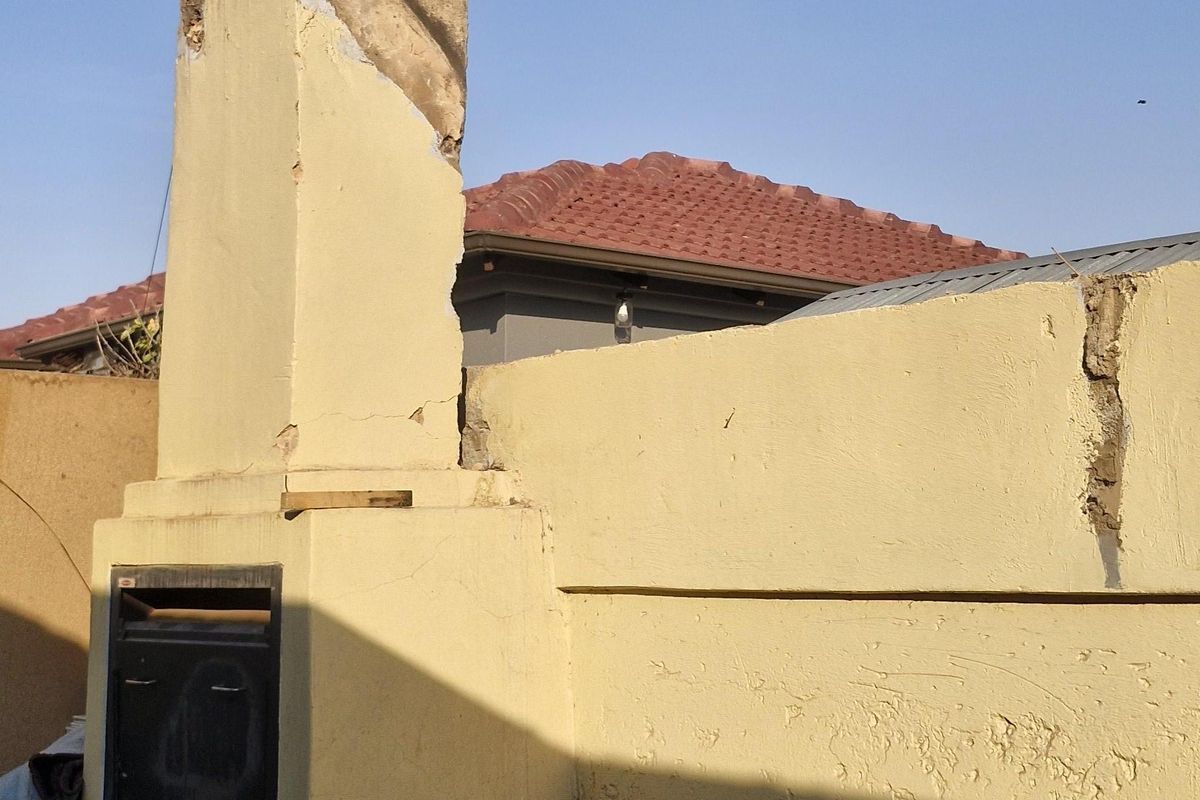 Rear outdoor area featuring a built-in braai and masonry chimney, showing significant signs of wear and structural plaster damage on the chimney and boundary wall.