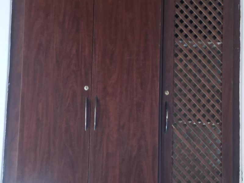 A built-in dark wood wardrobe featuring solid doors and a decorative lattice panel door, set against a wood-paneled ceiling.