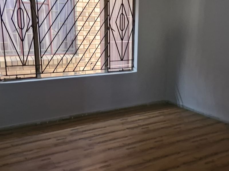 An empty bedroom featuring laminate flooring and security bars on the window, requiring minor cosmetic updates to the walls and skirting.