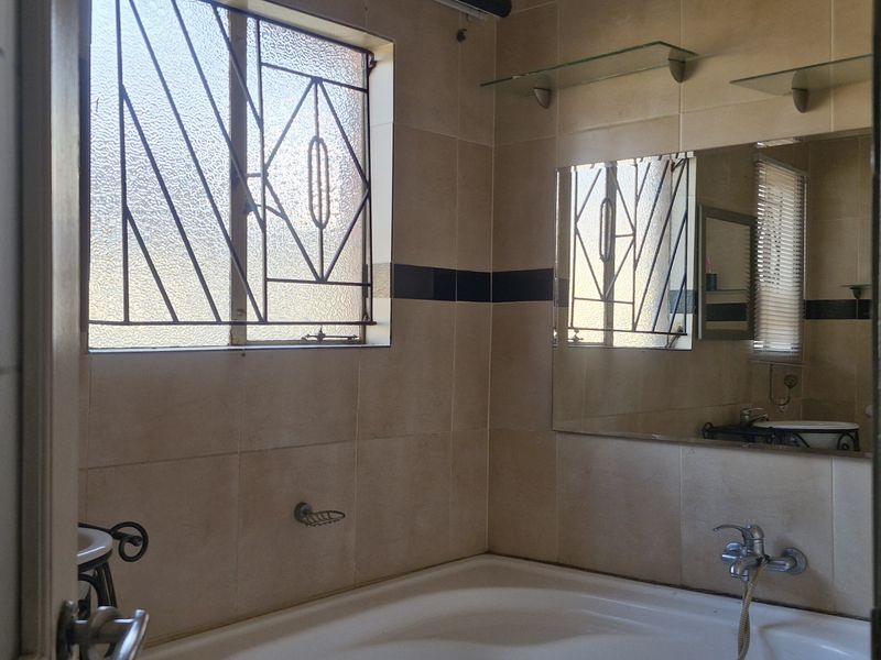 A functional bathroom featuring tiled walls, a built-in bathtub with wall-mounted fixtures, and a window with security bars.