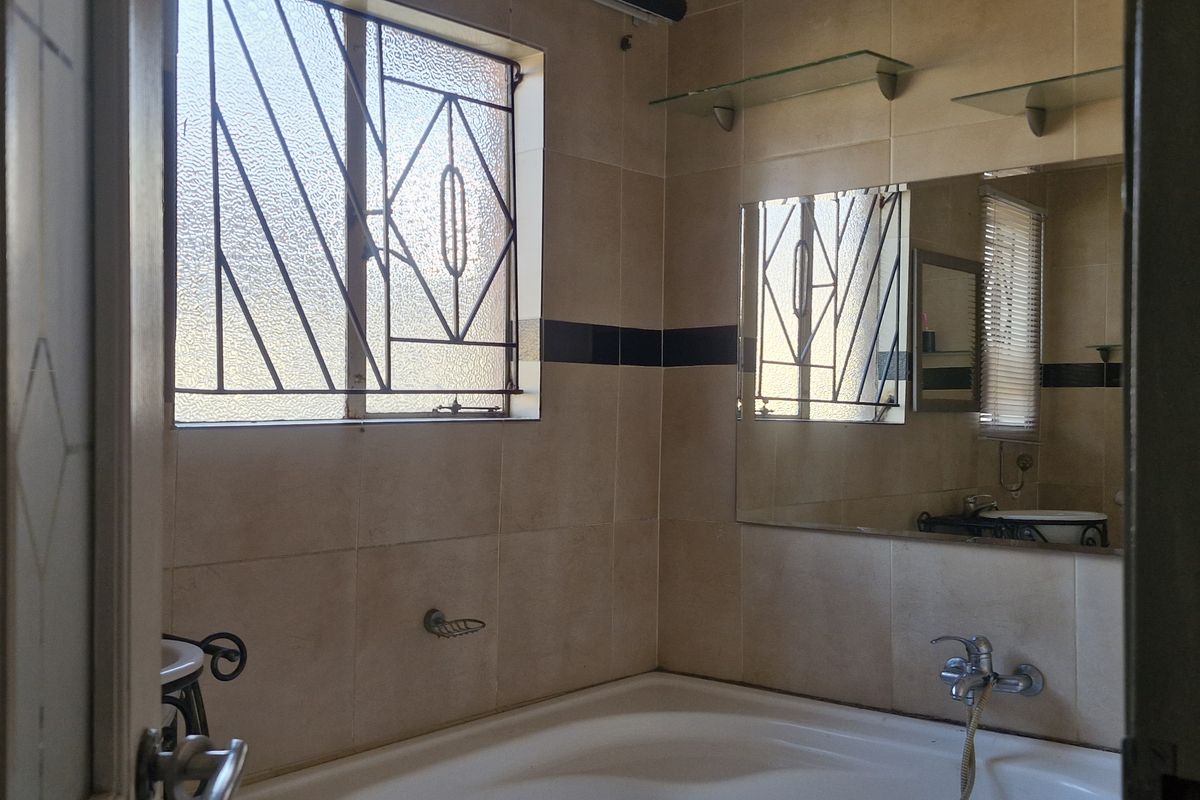 A functional bathroom featuring tiled walls, a built-in bathtub with wall-mounted fixtures, and a window with security bars.