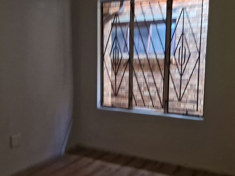 An empty bedroom featuring a window with security bars and basic wall finishes, suitable for renovation or staging.
