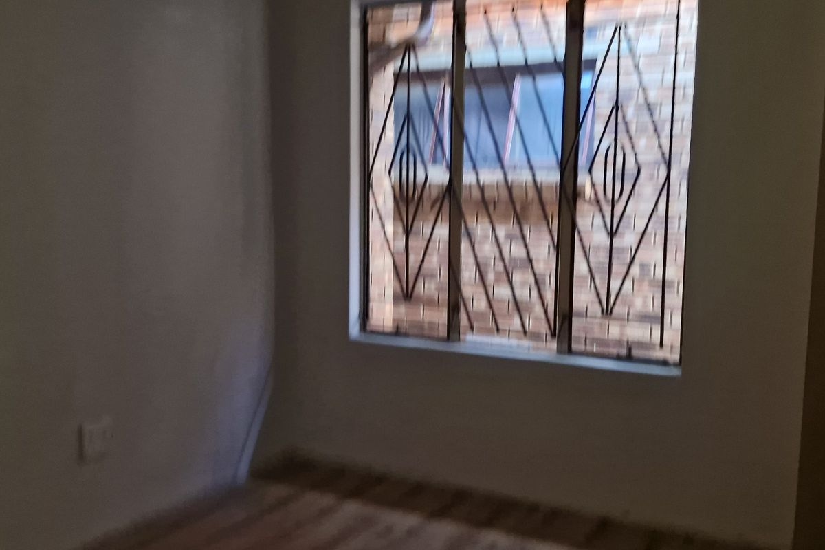 An empty bedroom featuring a window with security bars and basic wall finishes, suitable for renovation or staging.