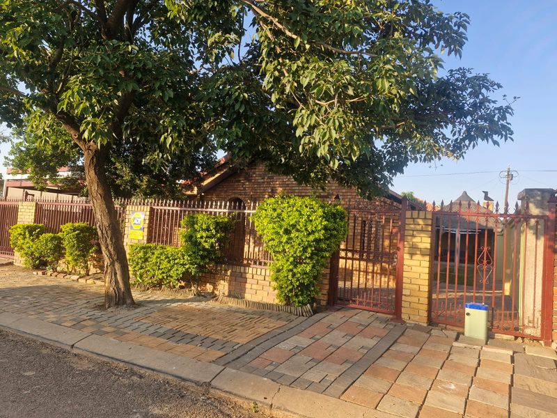 Front view of the property featuring a face brick facade, secure wrought iron fencing, and a paved driveway entrance.