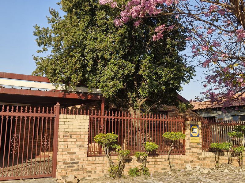 Front elevation of the property featuring a brick boundary wall, wrought iron security fencing, and a covered carport area.
