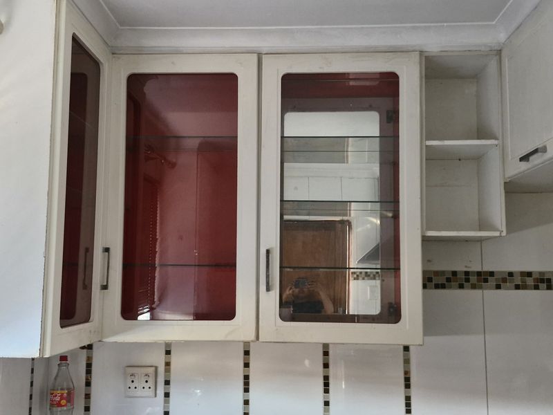 A close-up view of kitchen wall-mounted cabinetry featuring glass-fronted doors and a tiled backsplash, showing signs of wear and dated finishes.