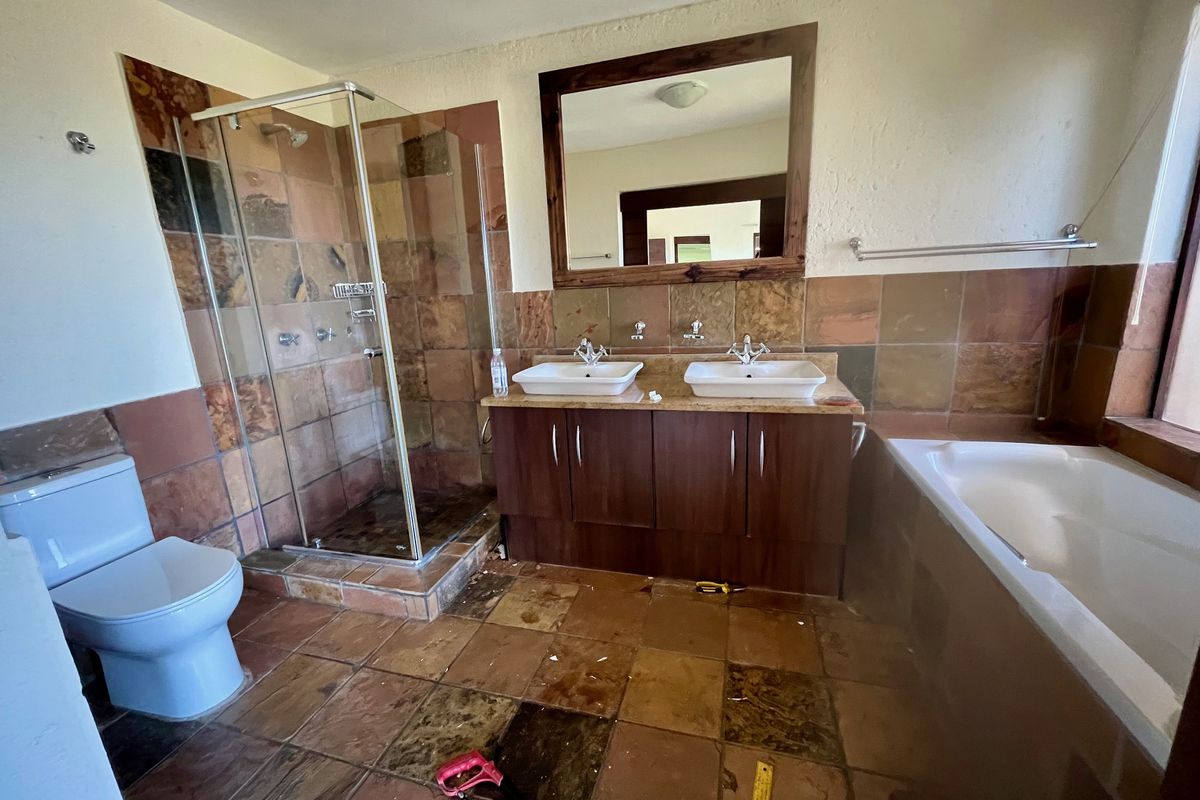 Spacious bathroom featuring a double vanity, glass-enclosed shower, and a built-in bathtub with natural stone-style wall and floor tiling.